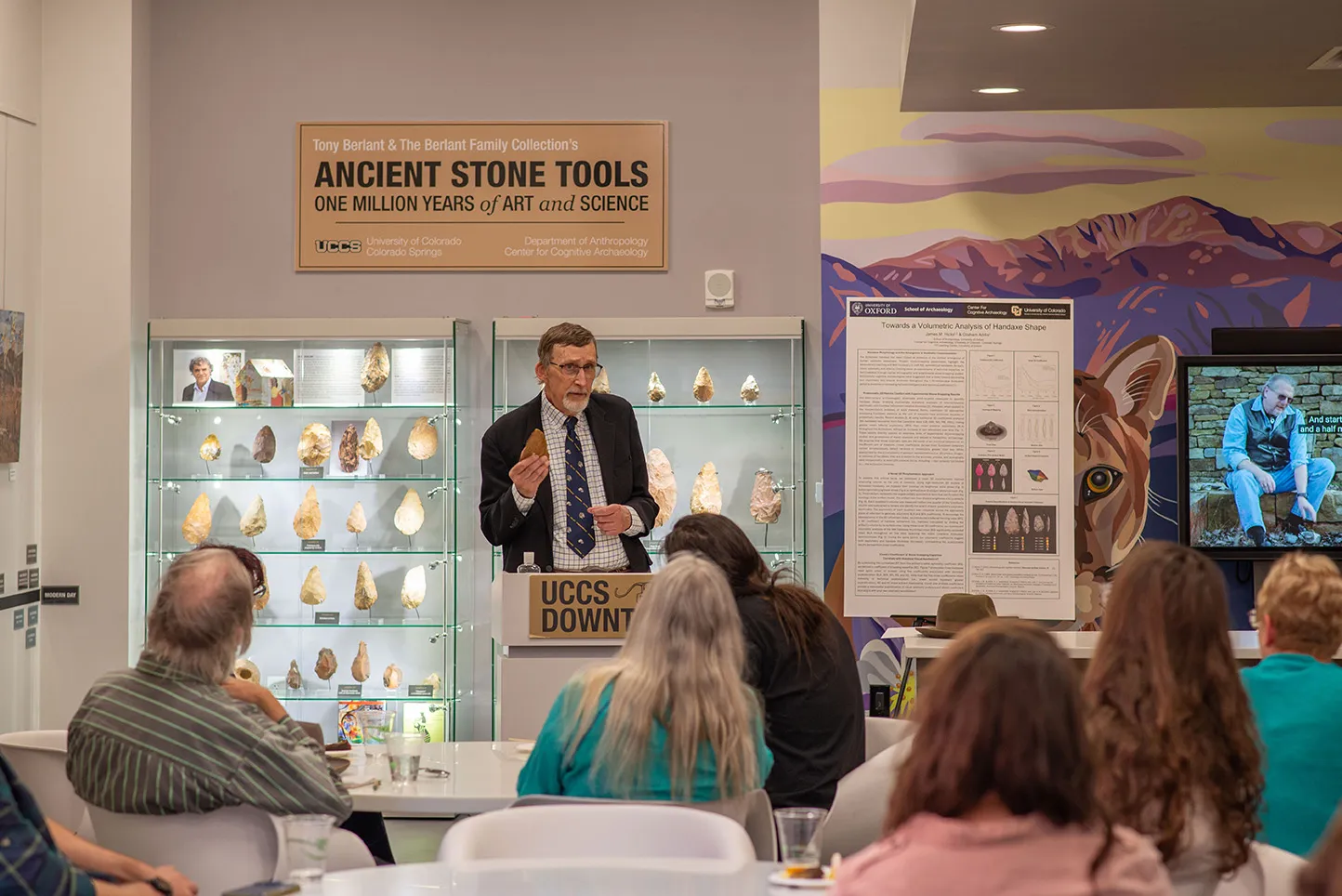 Person speaking in front of Ancient Stone Tools with listeners.
